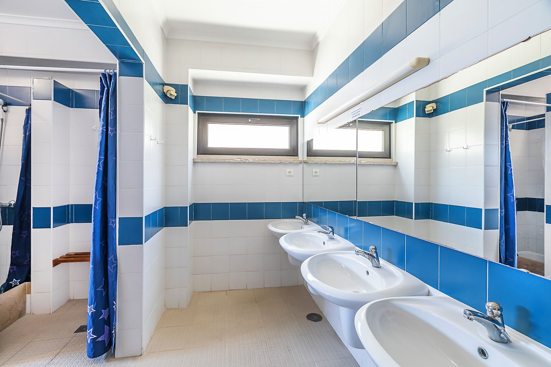 Un baño con cuatro lavamanos, ducha y ventana.