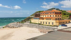A coastal building with a stone wall, a beach in the foreground, and the ocean in the background. - HI Areia Branca – Pousada de Juventude - Hostel (Lourinha)