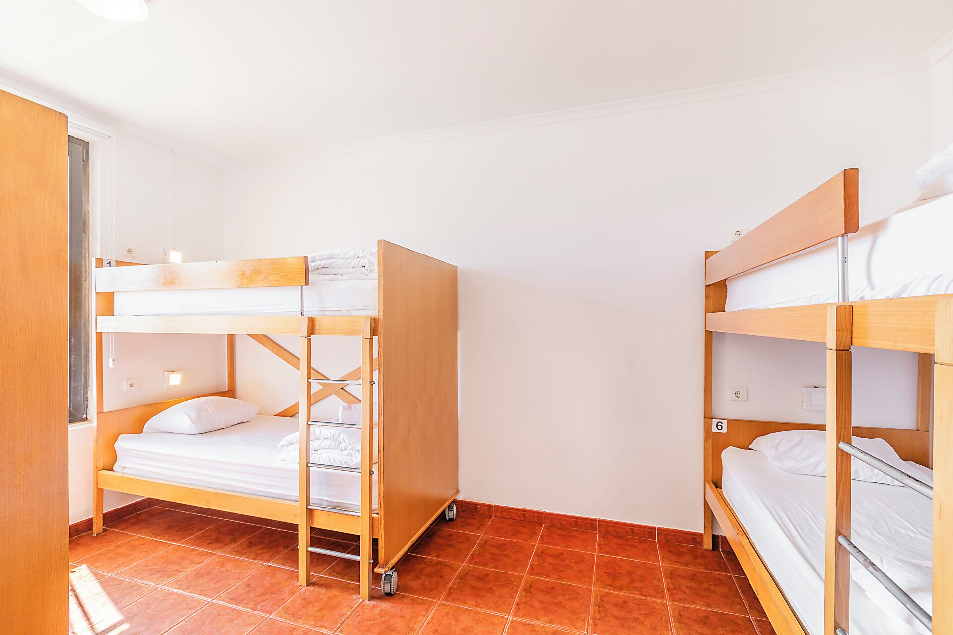 Een kleine, praktische kamer met twee stapelbedden, een houten garderobe en een betegelde vloer.