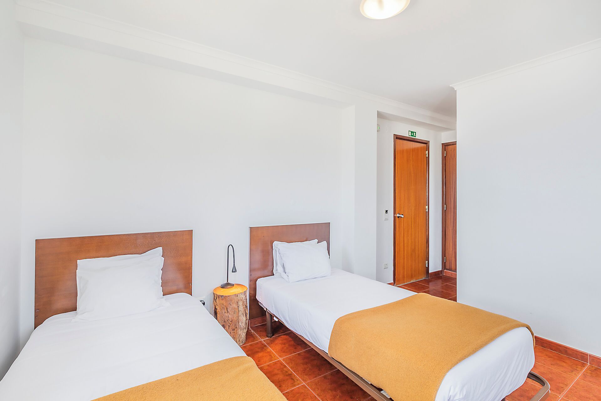 Ein Hotelzimmer mit zwei Betten, einem Holzkopfteil, einem Nachttisch und einer Tür mit Ausgangsschild.