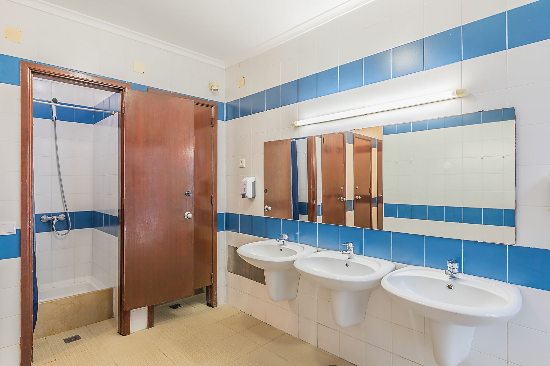 A public restroom with a shower, three sinks, and a large mirror.