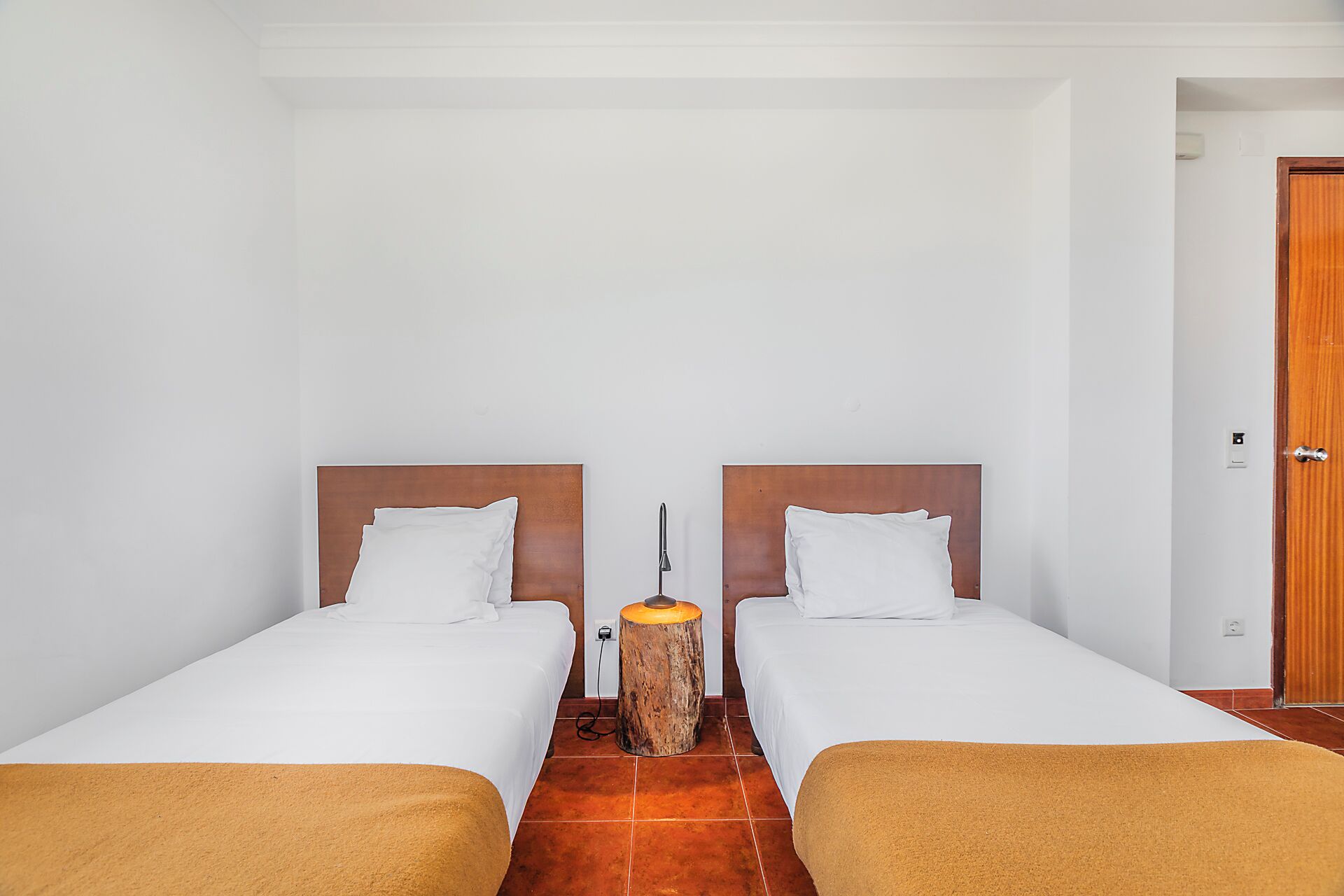 A room with two beds, a wooden nightstand, a small table, and a door.