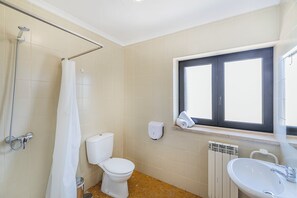 A bathroom with a toilet, a shower, a window, and a radiator. - HI Areia Branca – Pousada de Juventude - Hostel (Lourinha)
