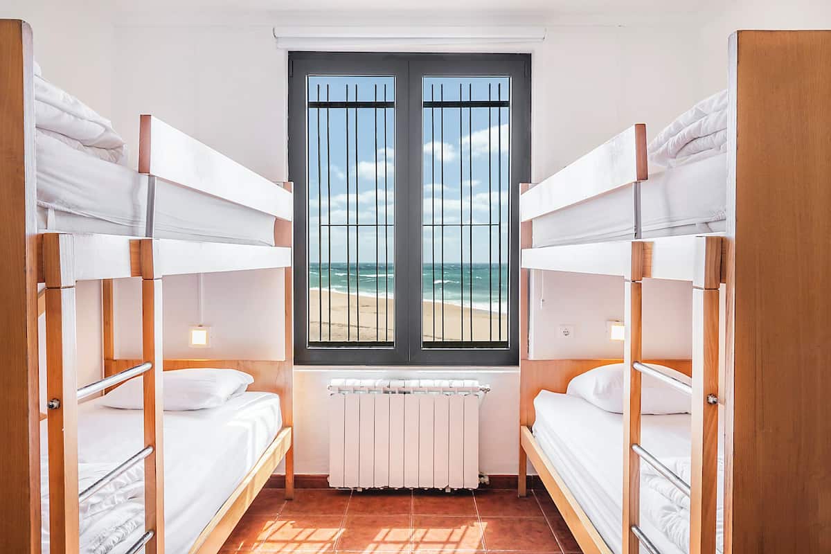 A room with bunk beds, a window with a view of the beach, and a radiator.