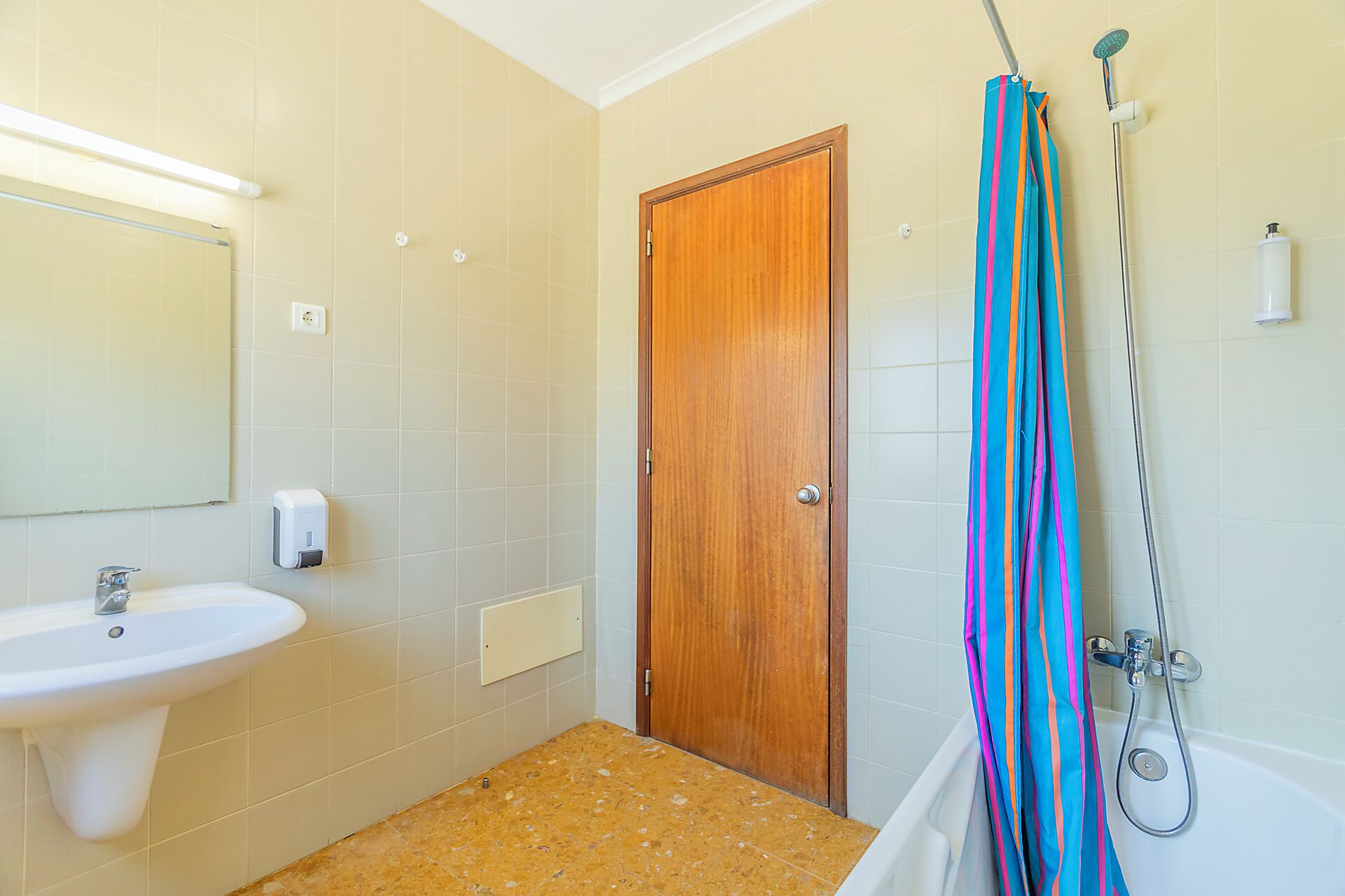 Un baño con lavamanos, puerta de madera, ducha y cortina de ducha a rayas.