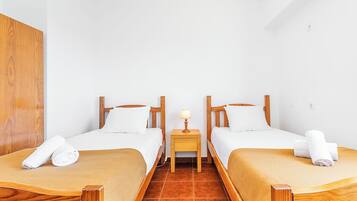Una camera d'albergo con due letti, testiere in legno, biancheria da letto bianca, un piccolo comodino con una lampada e un armadio in legno.
