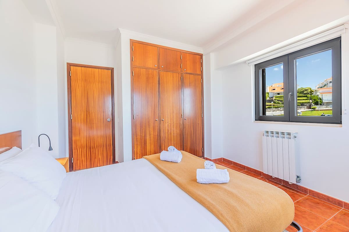 A hotel room with a bed, wooden wardrobe, window with a view, and a radiator.