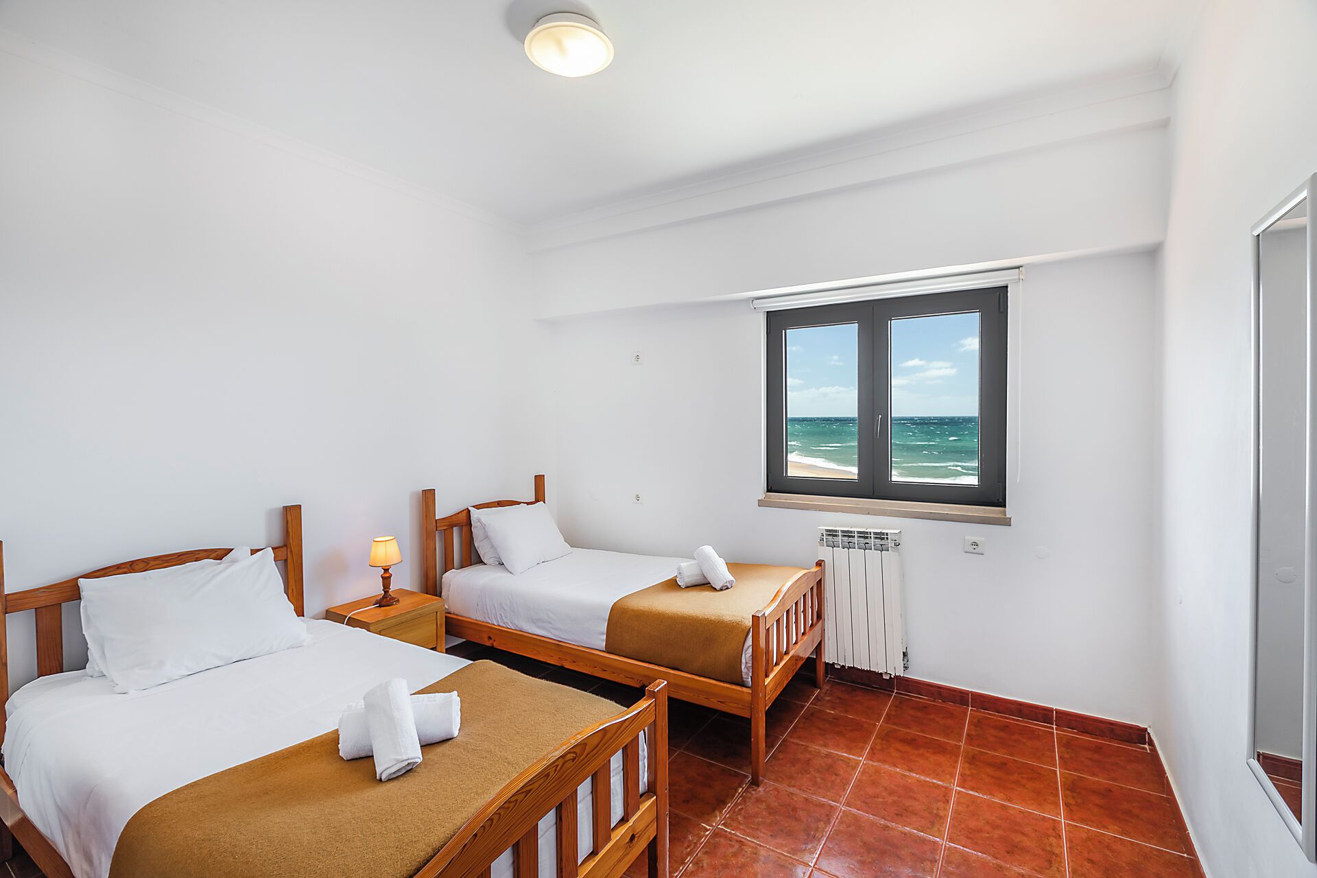 Una habitación con dos camas de madera, una ventana con vista al mar y suelo de baldosas.