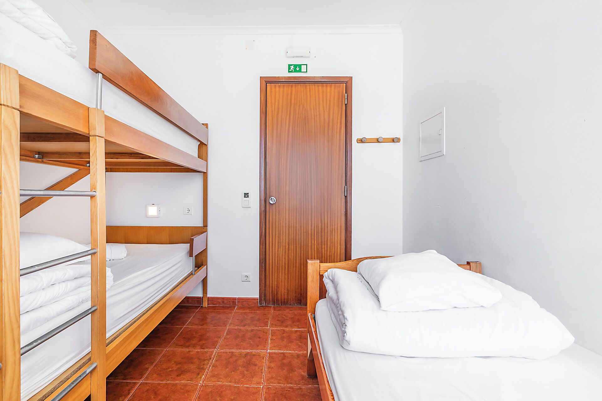 Een kamer met stapelbedden, een houten deur en een eenpersoonsbed.