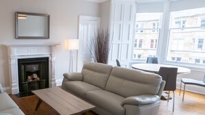 Un salon avec une cheminée, un canapé, une table basse et un coin repas comprenant une table et des chaises.
