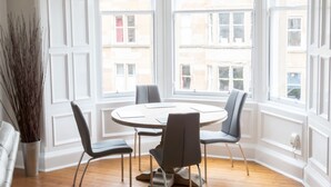 Un coin repas avec une table ronde, quatre chaises et une vue sur les bâtiments grâce à de grandes fenêtres.