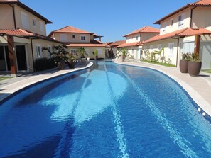 Une piscine à bord incurvé, entourée de bâtiments aux toits recouverts de tuiles rouges et aux murs de couleur beige.