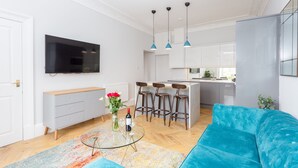 Una sala de estar moderna con un sofá azul, una mesa de centro de vidrio y un televisor montado en la pared.