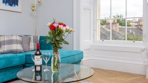 Una sala de estar con una mesa de centro de vidrio, una botella de vino y un jarrón de flores.