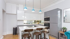 Una cocina moderna con armarios blancos, una isla central con taburetes, un lavamanos de acero inoxidable, un microondas y un refrigerador.