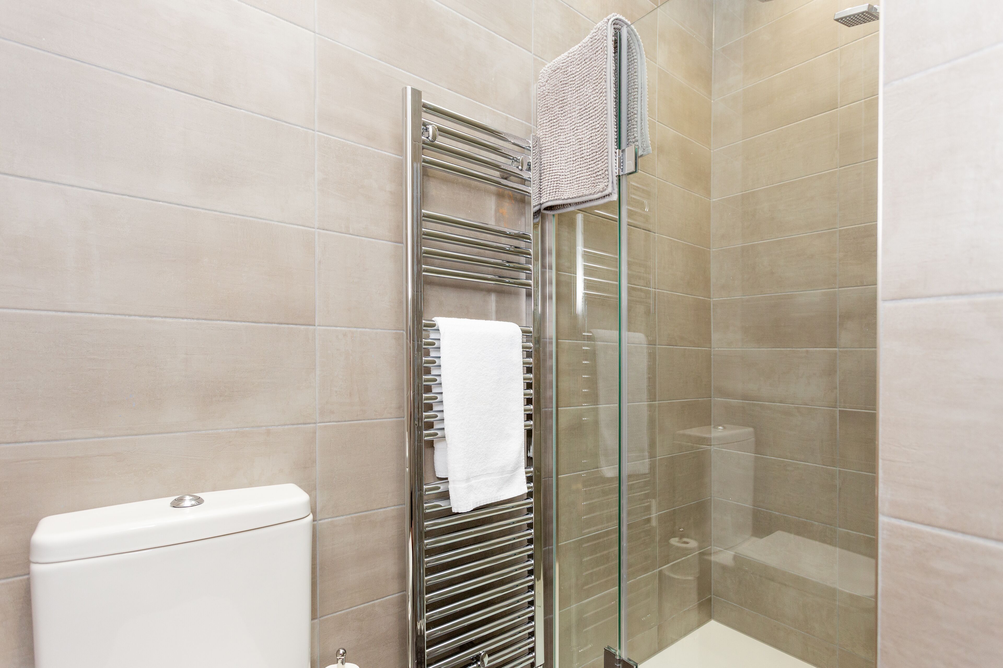 Un bagno moderno con cabina doccia in vetro, un portasciugamani con un asciugamano bianco e un water.
