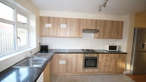 A kitchen with wooden cabinets, a stainless steel sink, a microwave, a stove, and a refrigerator. - Flexistay Hillbrook (London)