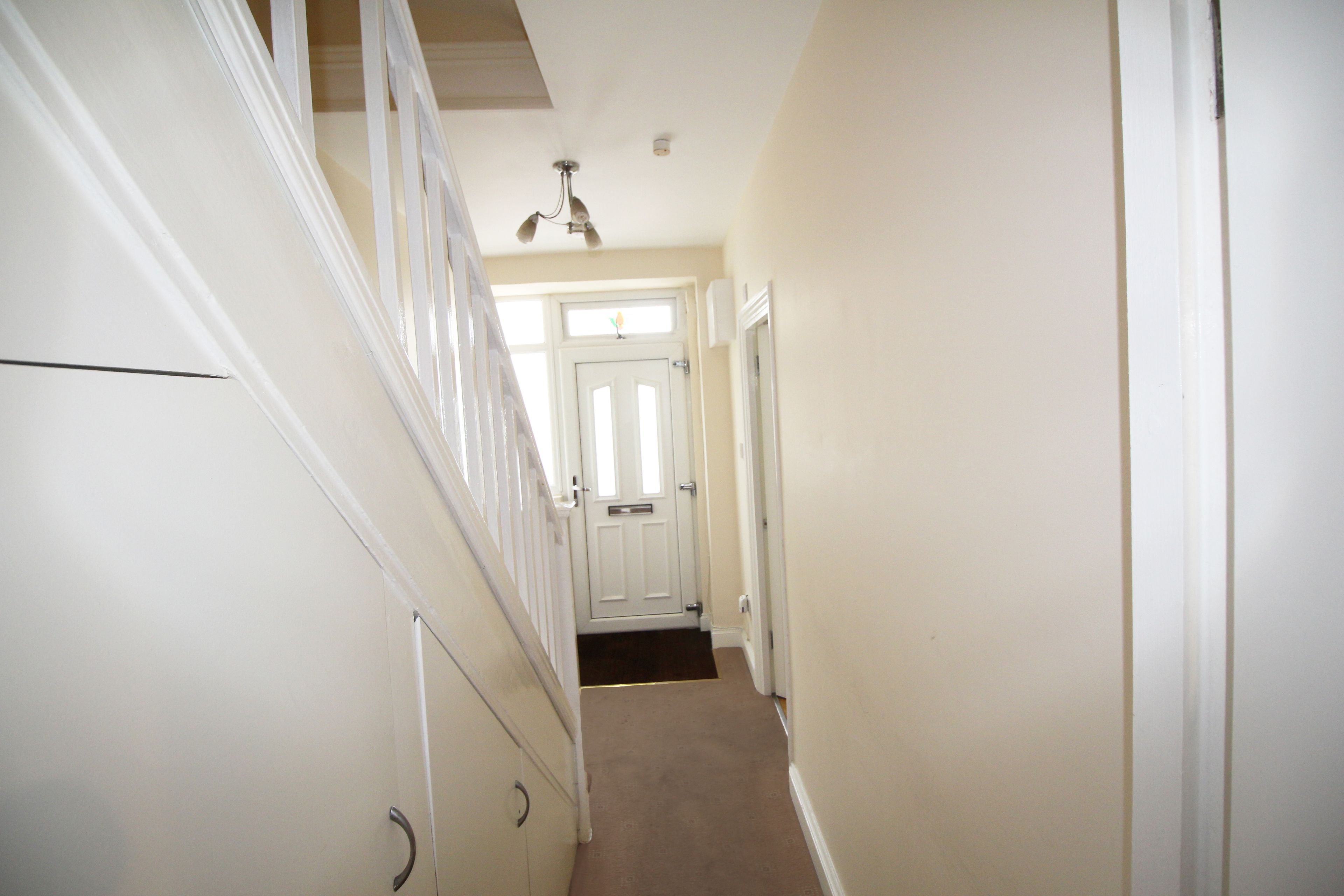 A narrow hallway with a carpeted floor, white walls, and a white door at the end.