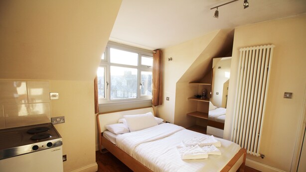A bedroom with a bed, a window, a radiator, and a kitchenette. - Flexistay Hillbrook (London)