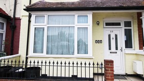 A two-story house with a white front door, a bay window, and a black metal fence. - Flexistay Hillbrook (London)