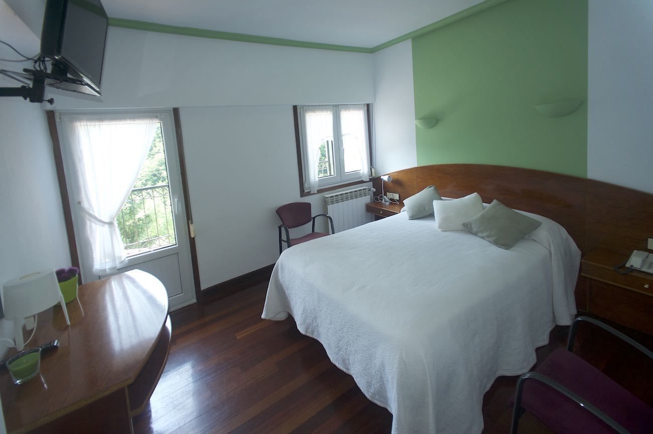 A hotel room with a wooden bed, a desk, a chair, and a television mounted on the wall.