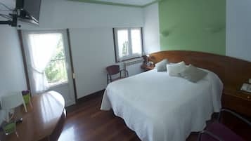 A hotel room with a wooden bed, a desk, a chair, and a television mounted on the wall.
