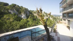 Un espace piscine offrant une vue sur un paysage montagneux, avec un arbre au premier plan et un bâtiment doté de balcons.
