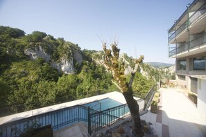 A pool area with a view of a mountainous landscape, a tree in the foreground, and a building with balconies. - Hotel Sindika (Oñati)
