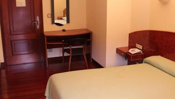 A hotel room with a bed, a desk, a chair, a telephone, and a mirror.
