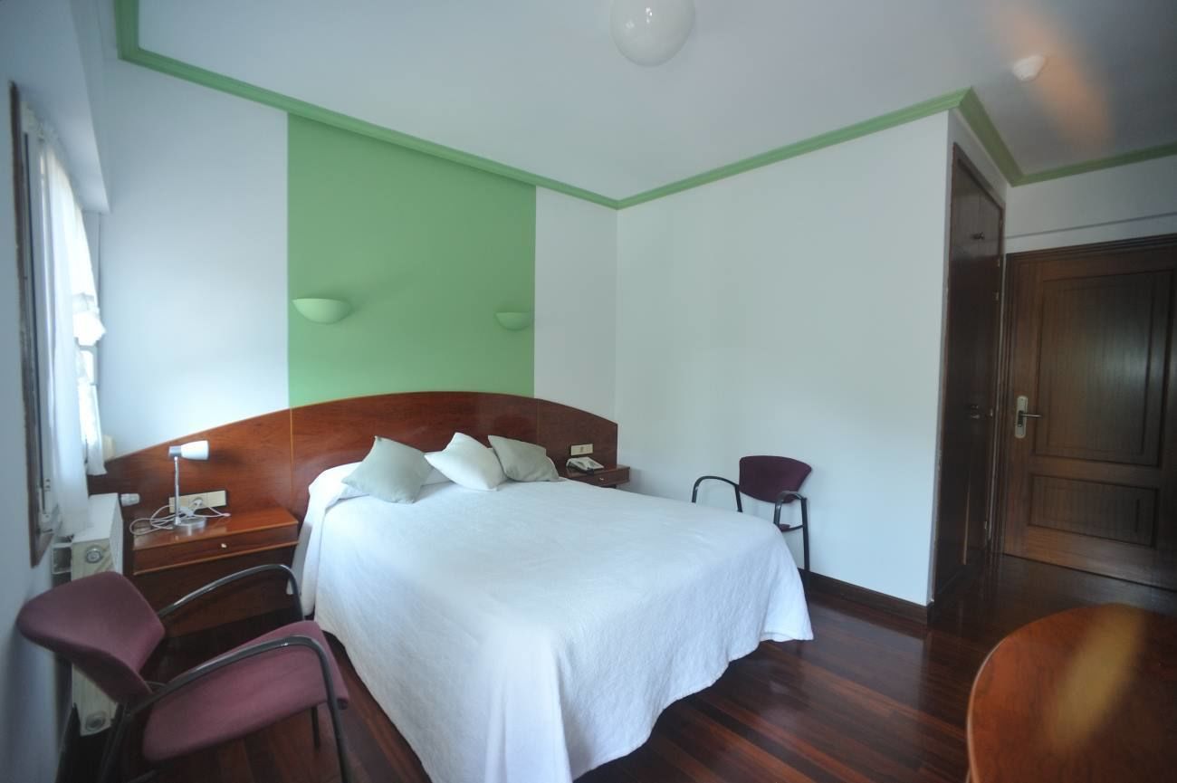 A hotel room with a large bed, a wooden headboard, a bedside table with a lamp, a chair, and a wardrobe.