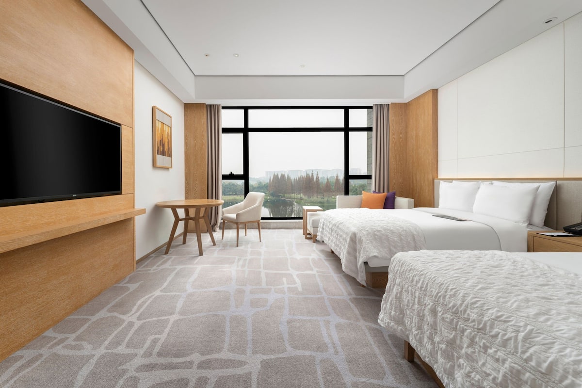A hotel room with a large TV, two beds, a desk, and a chair.