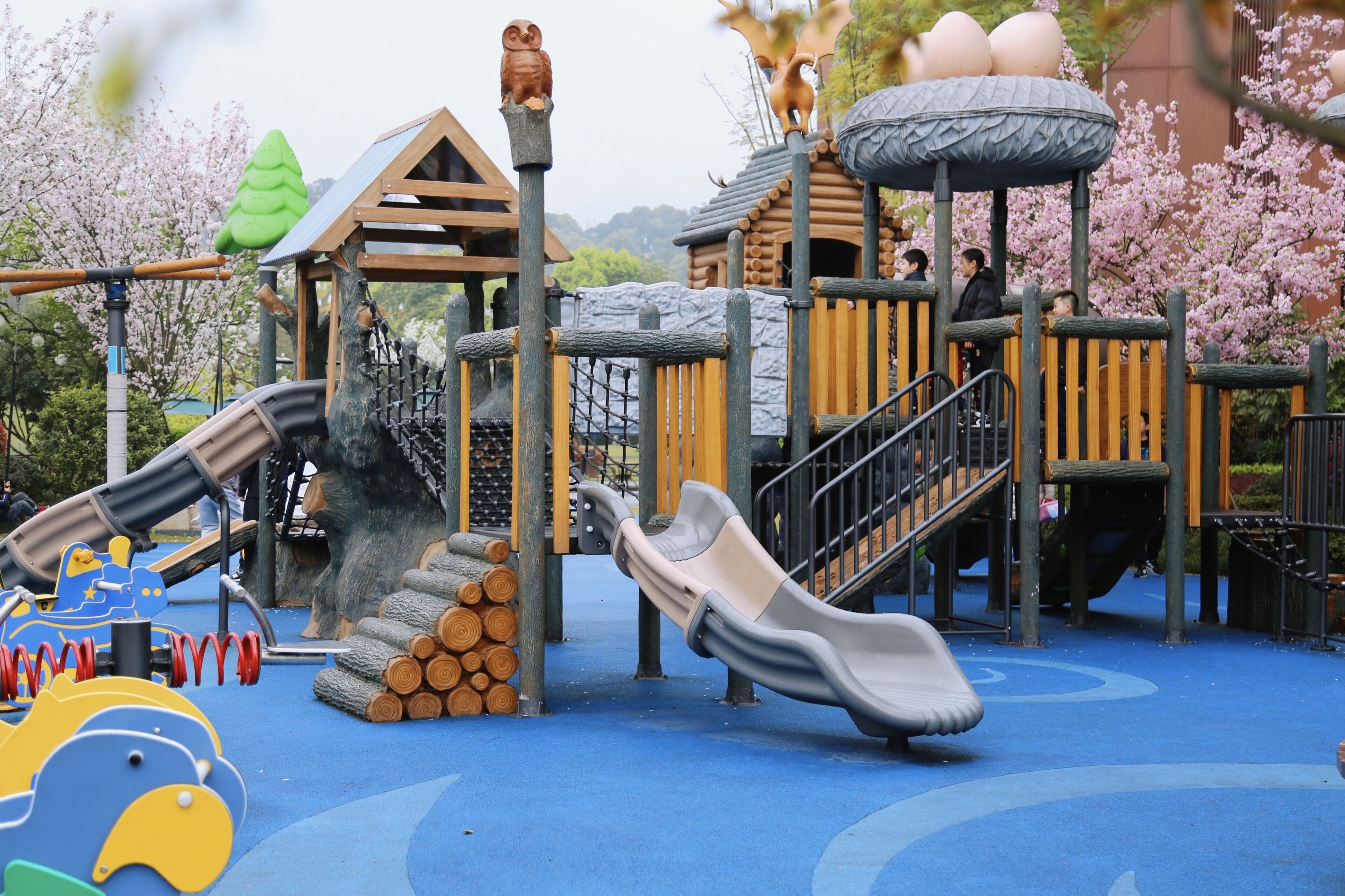 A children's playground with slides, climbing structures, and a wooden playhouse.
