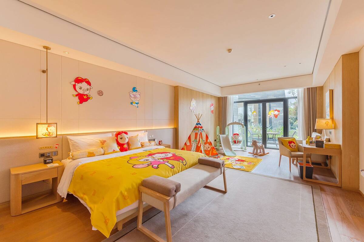 A hotel room with a bed, bedside table, lamp, and a view of the outdoors.