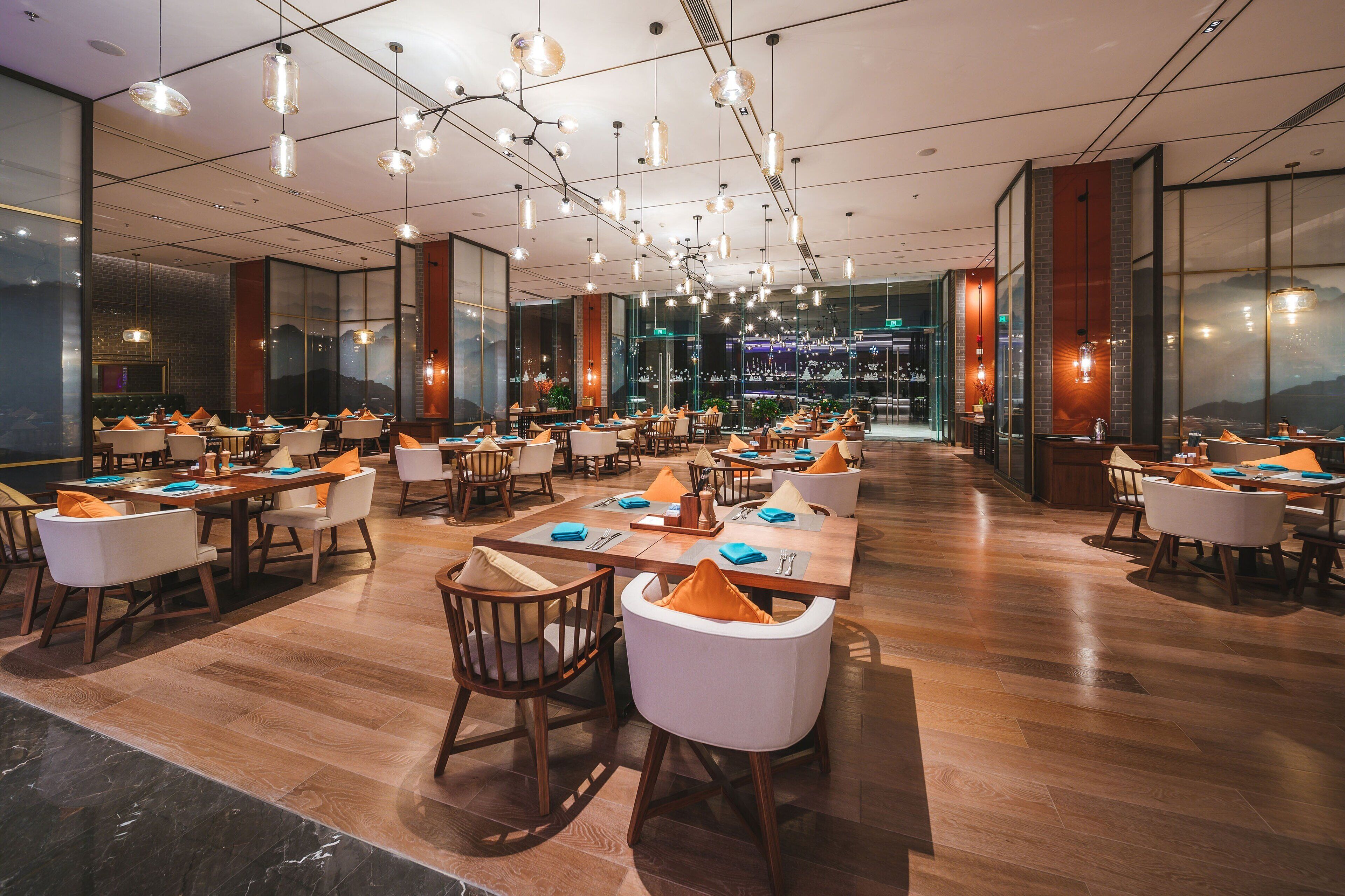 A spacious dining area with multiple tables and chairs, modern pendant lighting, and large windows offering views of the cityscape.
