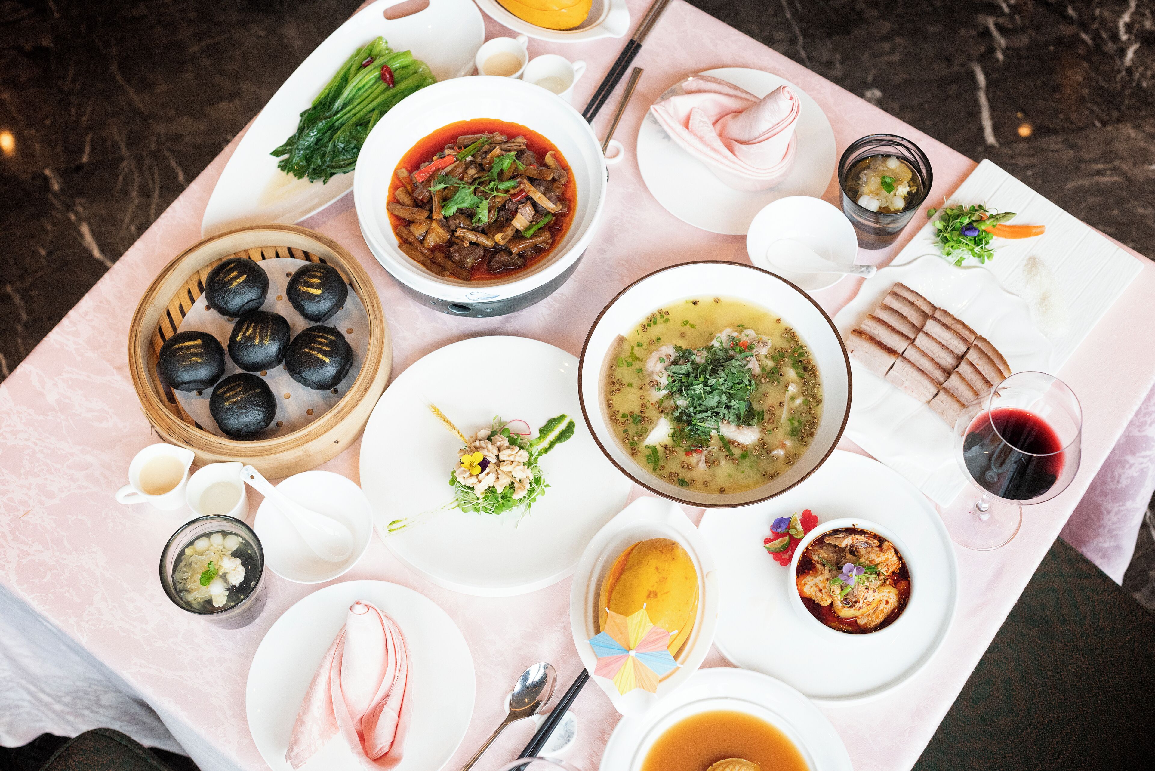 Una mesa con varios platos, incluyendo dim sum, sopa y una copa de vino tinto.