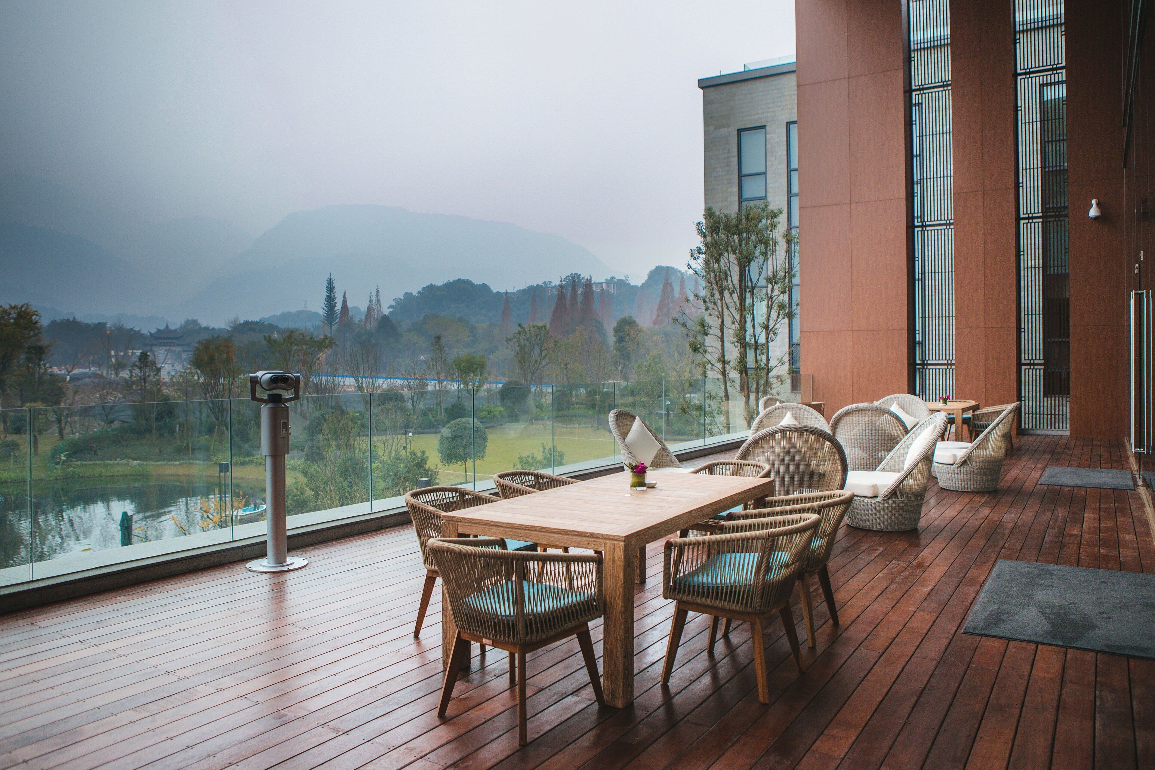 Una terraza de madera con mobiliario de mimbre que da a un lago y montañas.