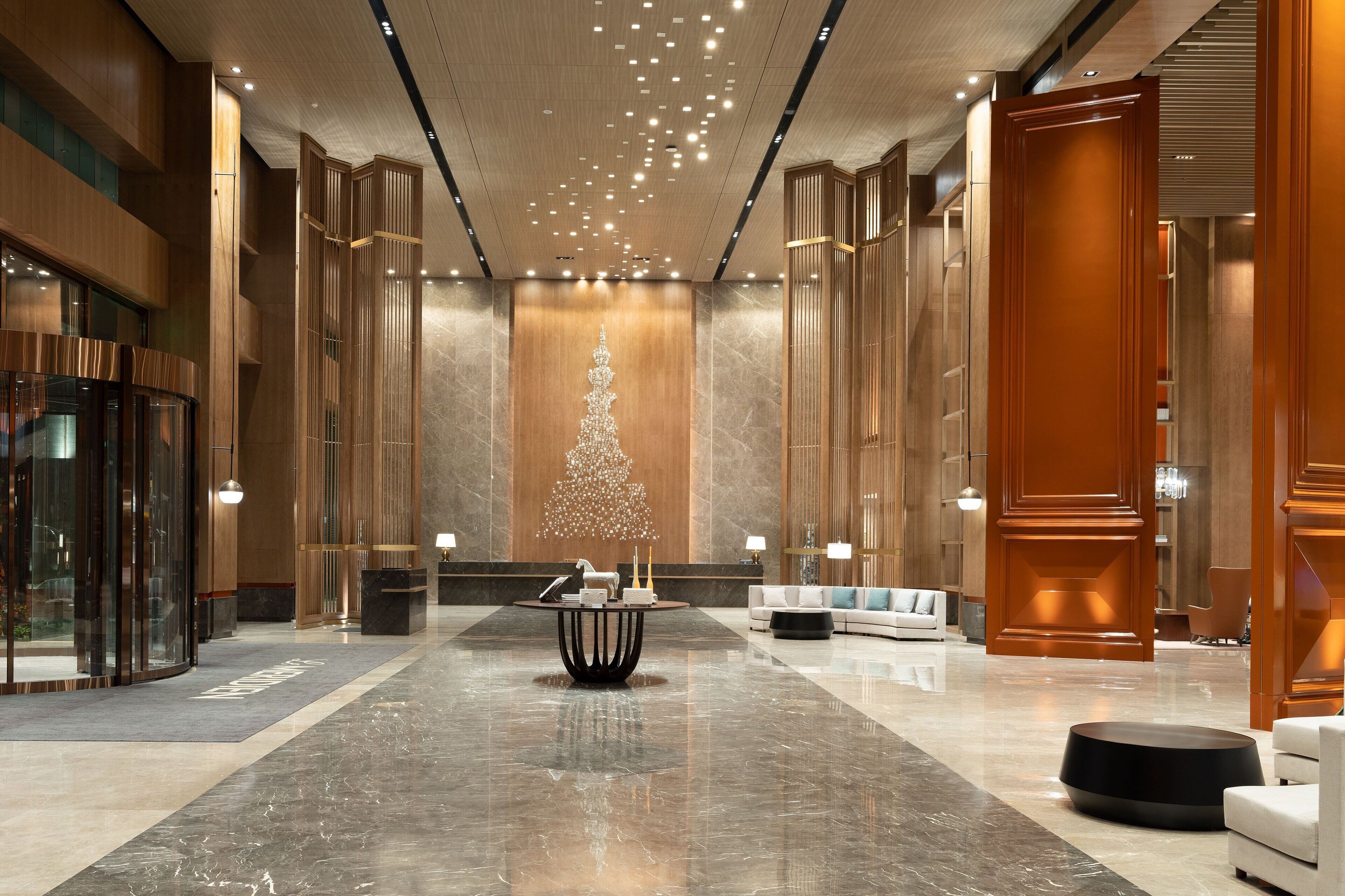 A spacious lobby with a central chandelier, a reception desk, and a seating area with sofas and a coffee table.