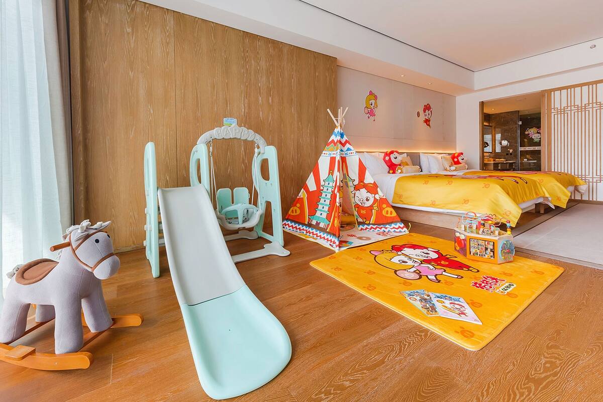 A child's playroom with a slide, rocking horse, and a bed with a colorful bedspread.