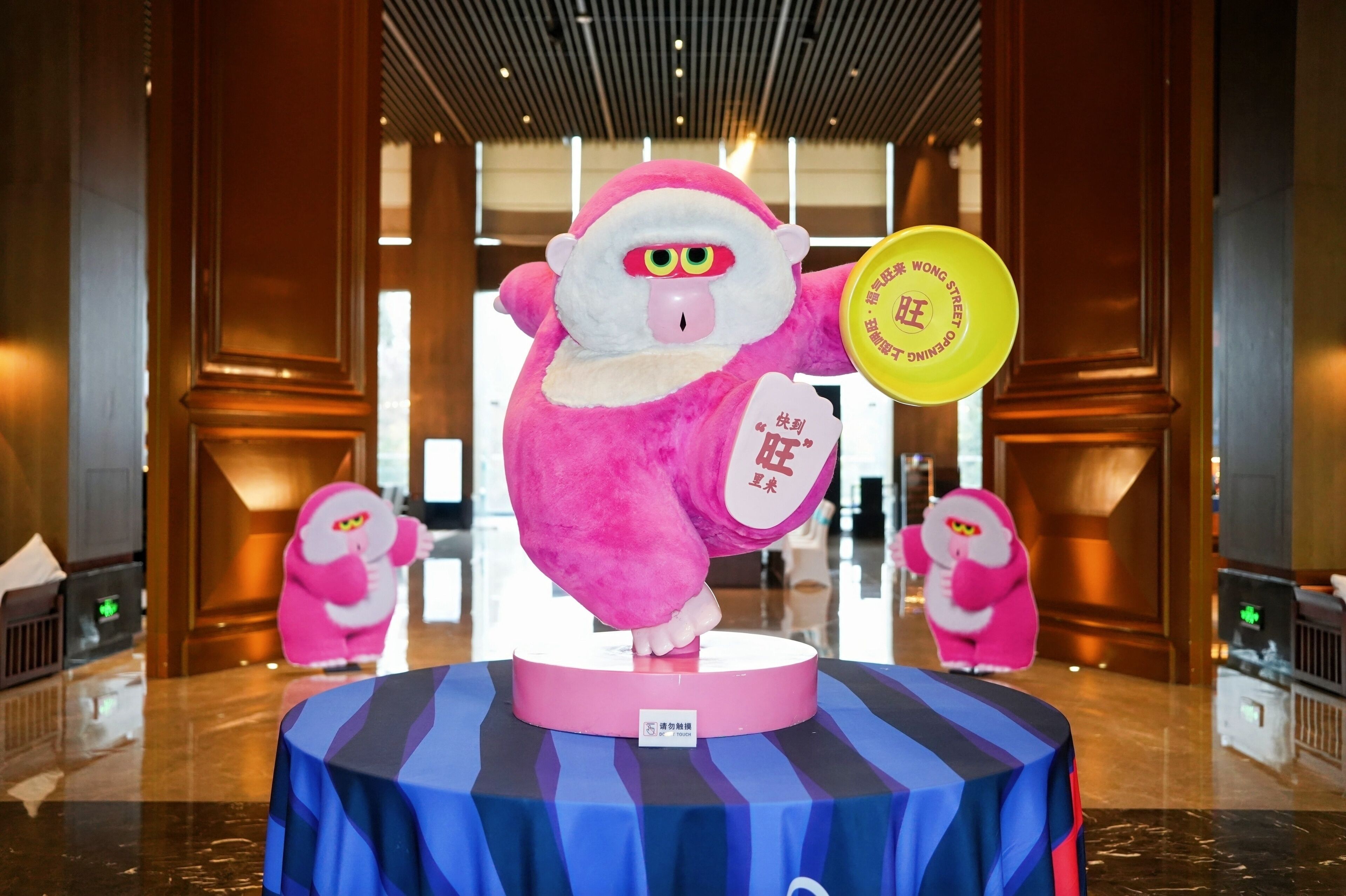 A plush Santa Claus figure holding a yellow sign, standing on a circular platform with a blue and black striped tablecloth.