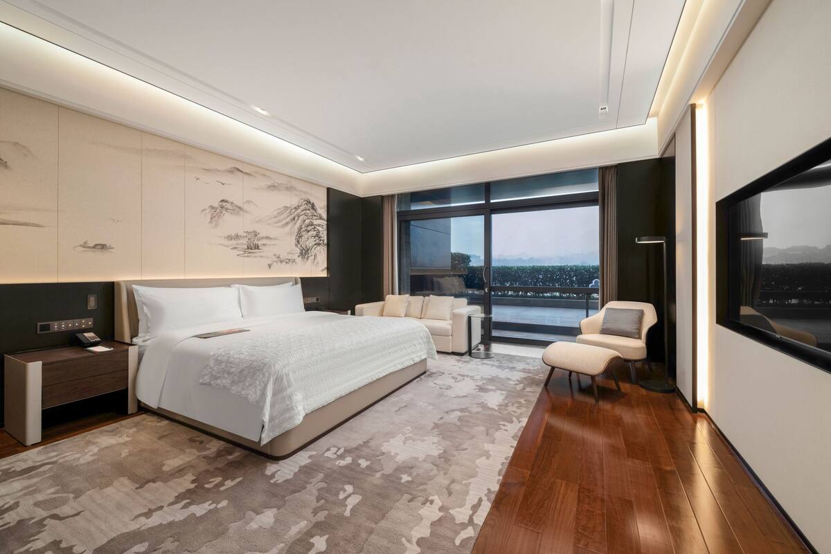 A modern bedroom with a large bed, a nightstand, a sofa, and a TV.