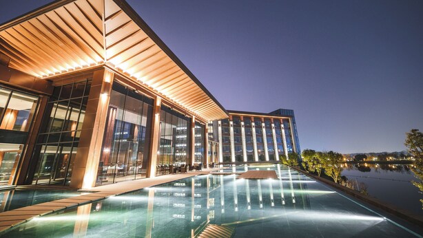 A modern hotel with a large pool, glass facade, and a waterfront view. - Le Méridien Emei Mountain Resort (Leshan)