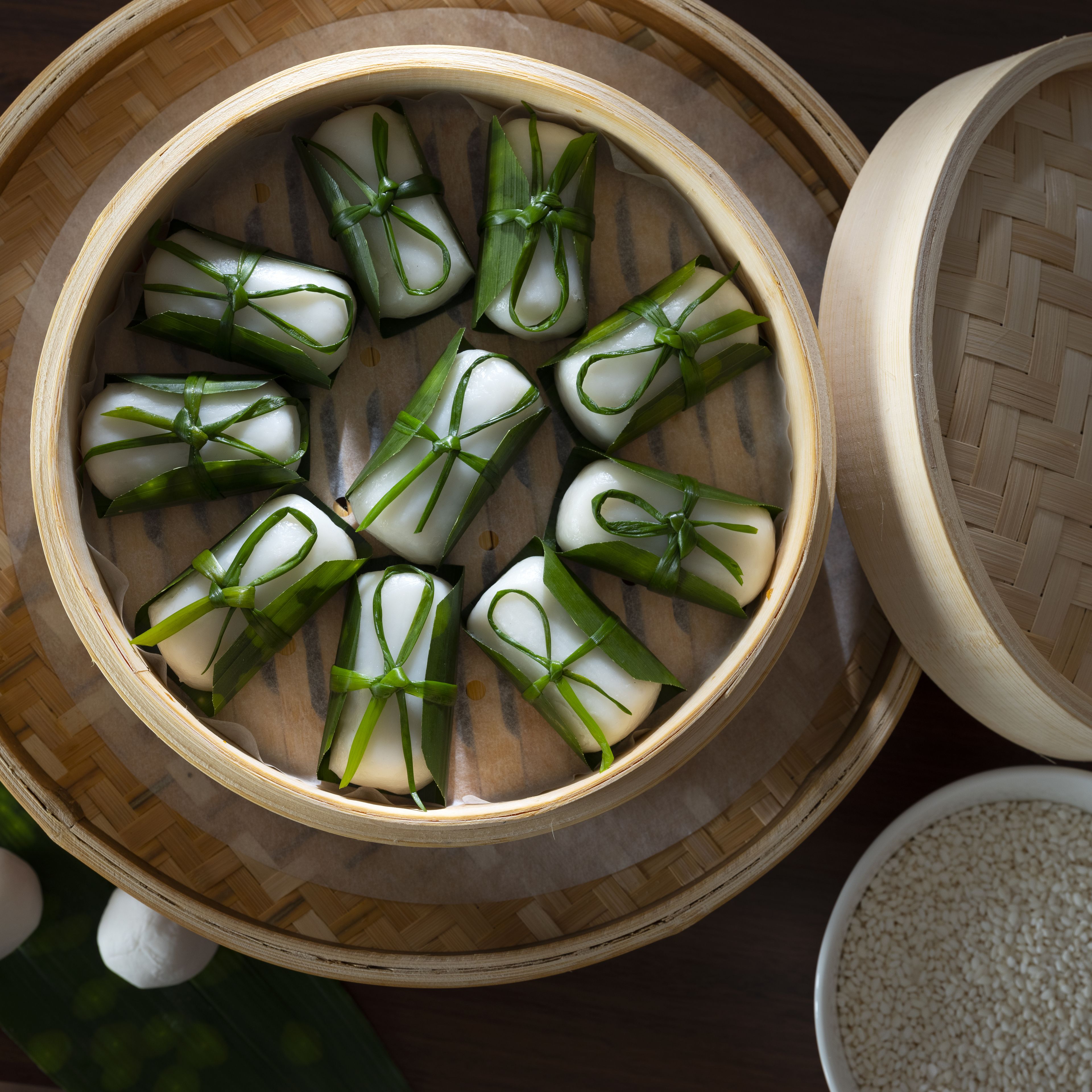 A bamboo steamer with several white, round, and tied items, likely food, on a woven mat.