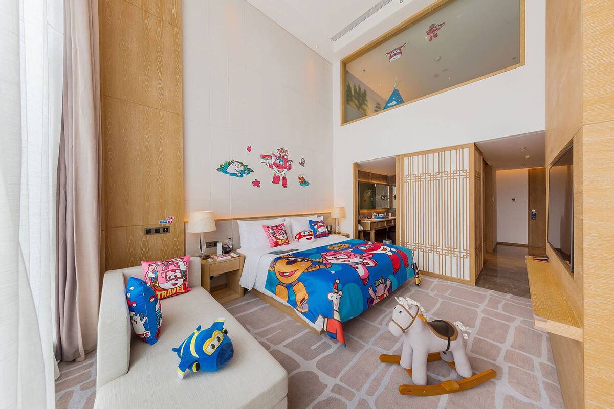 A hotel room with a large bed, a sofa, a rocking horse, and a TV.