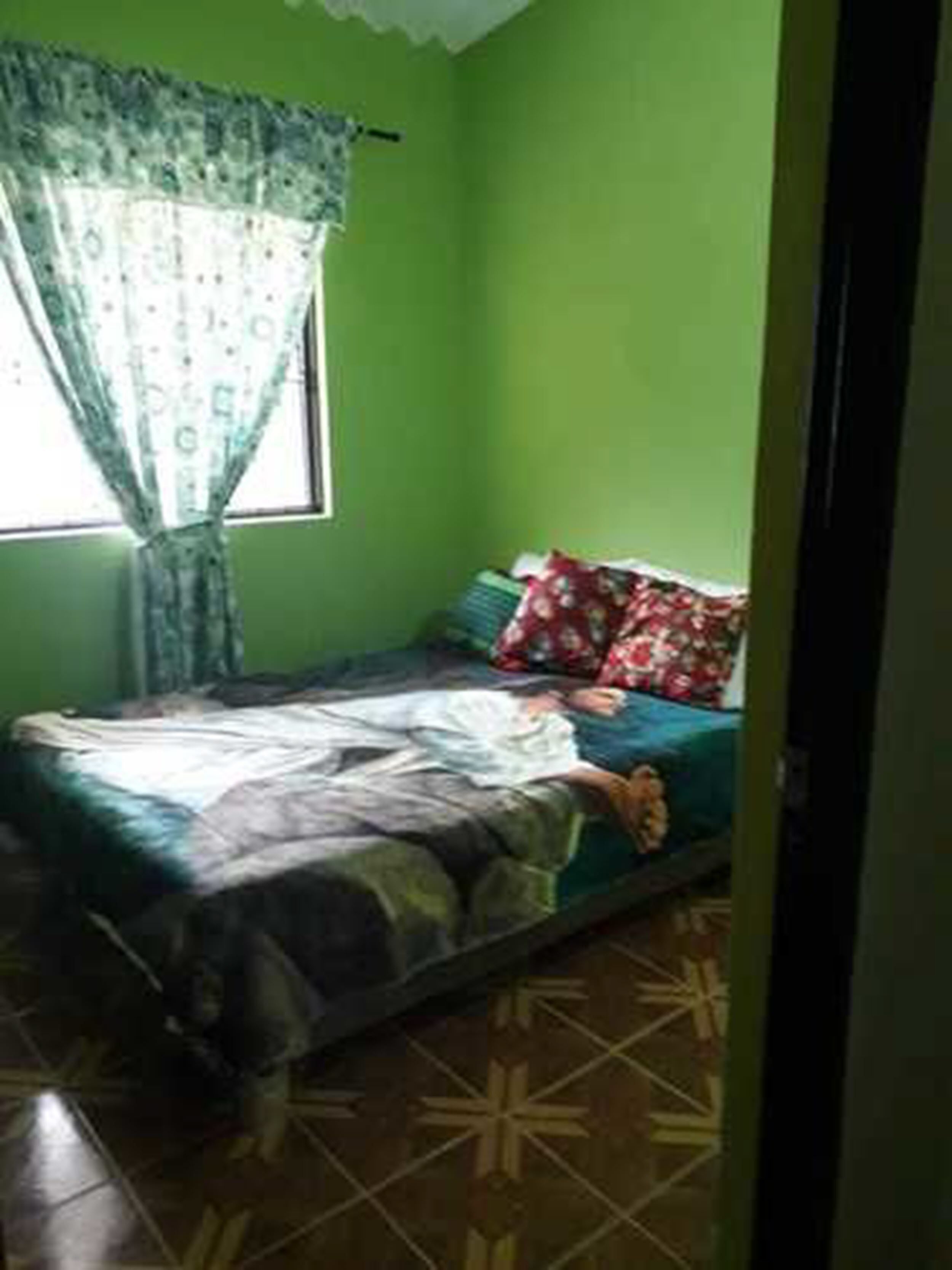 A small room with a bed, a window with curtains, and a green wall.