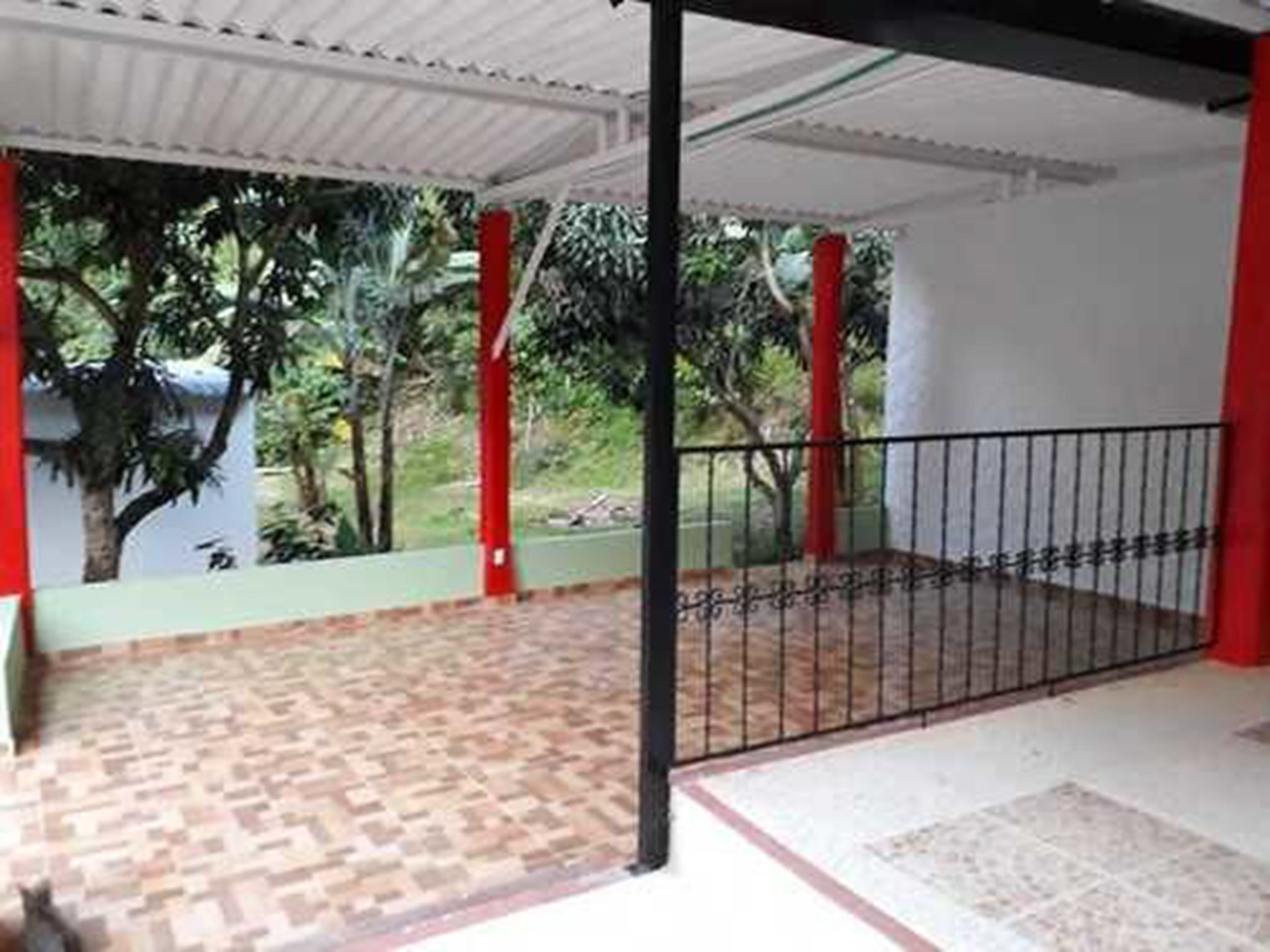 A covered outdoor area with a patterned floor, a metal gate, and red pillars.