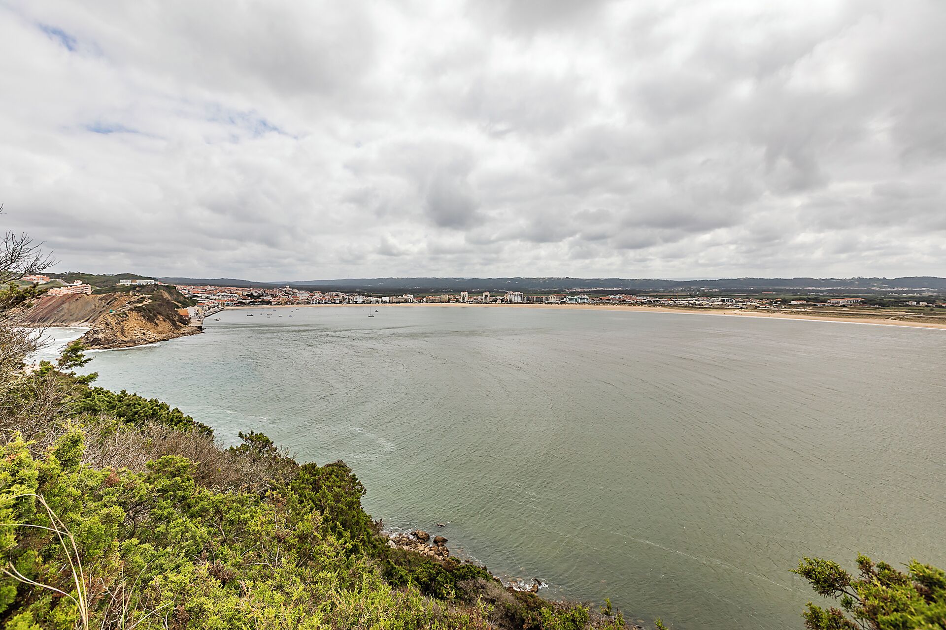 A coastal view with a wide beach, a calm sea, and a distant town.