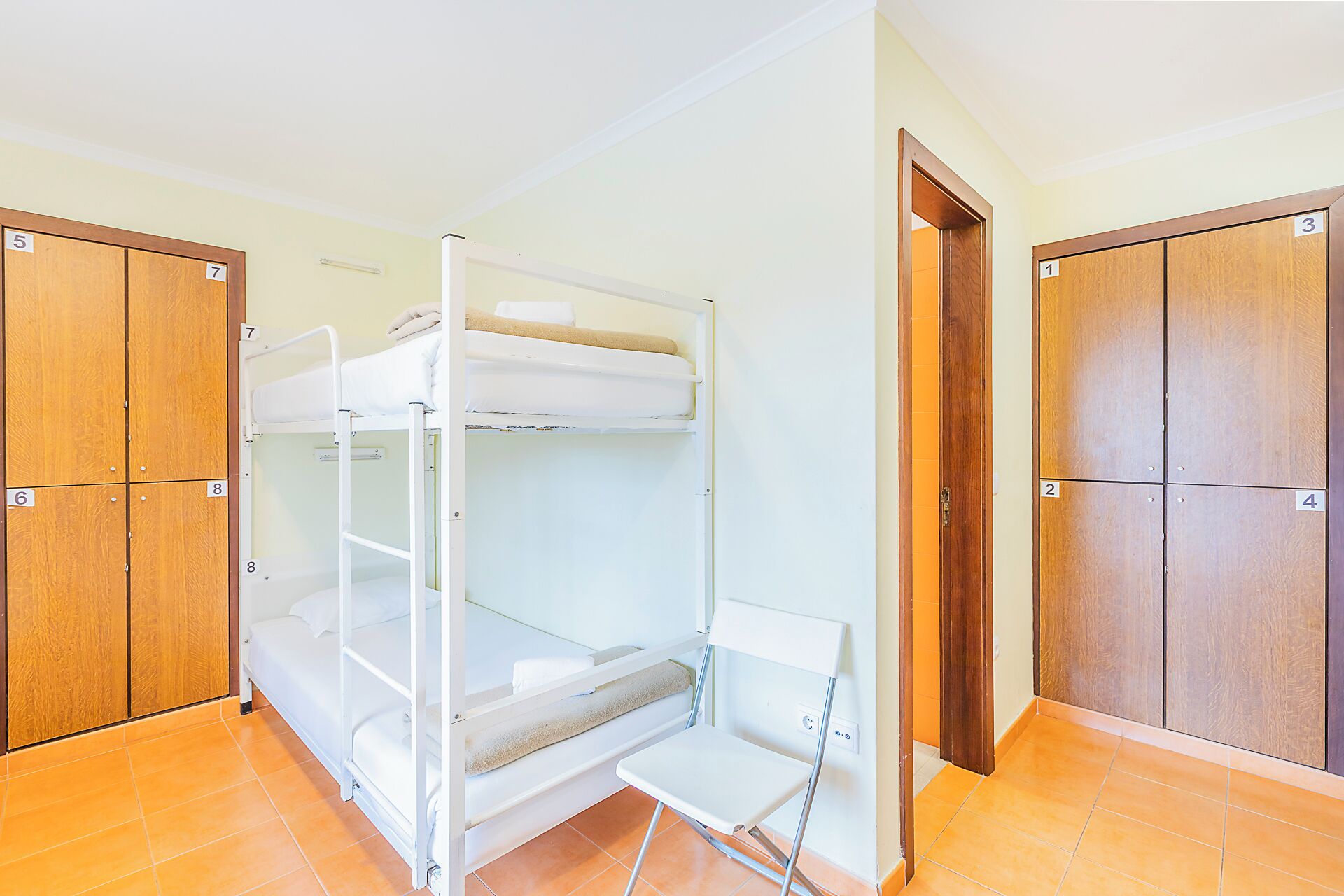 A room with bunk beds, a chair, and wooden wardrobes.