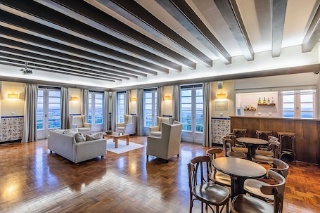 A spacious hotel lobby with a high ceiling, large windows, and a bar area.. HI Alfeizerão - Pousada de Juventude - Hostel