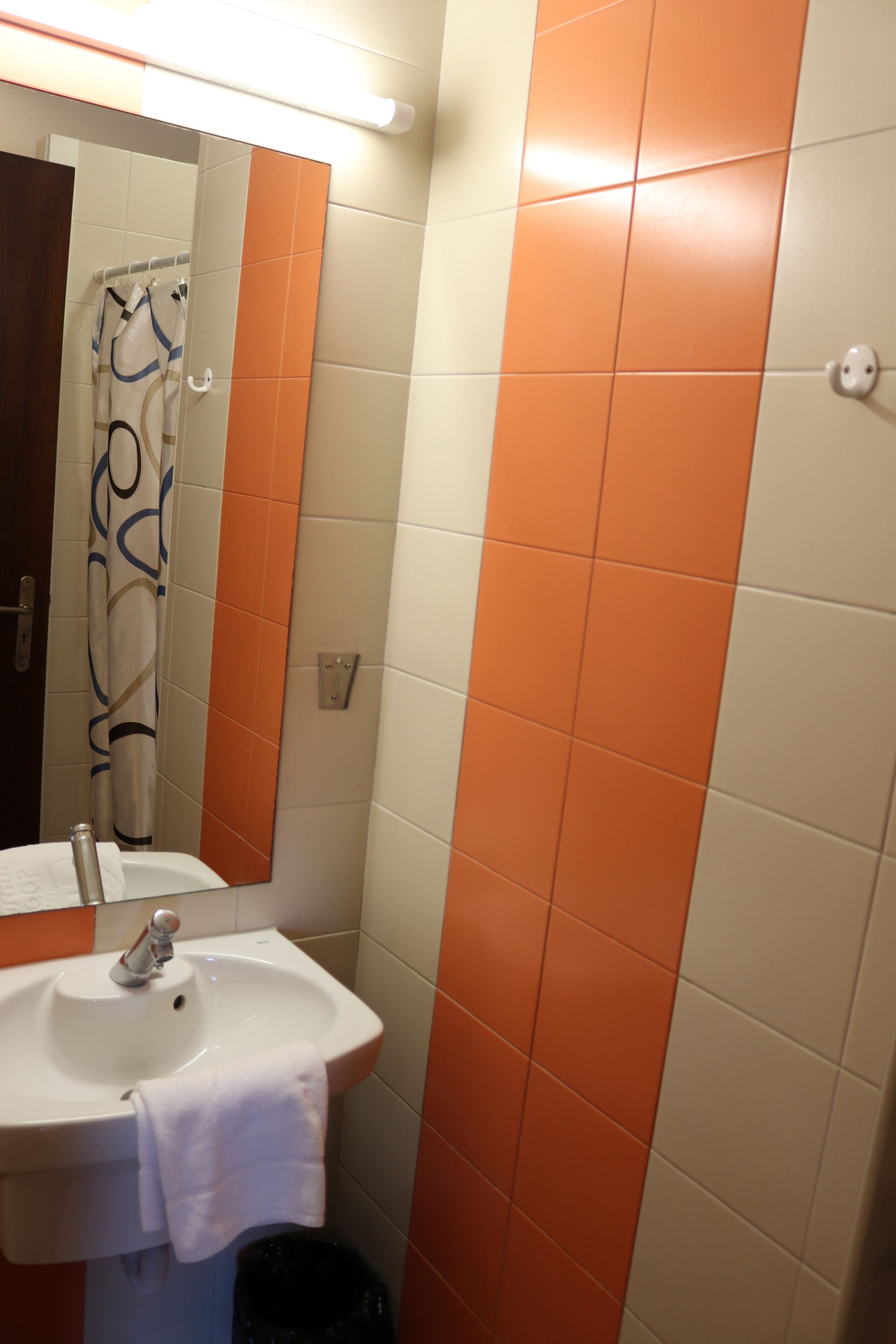 A bathroom with a sink, mirror, and orange-tiled walls.