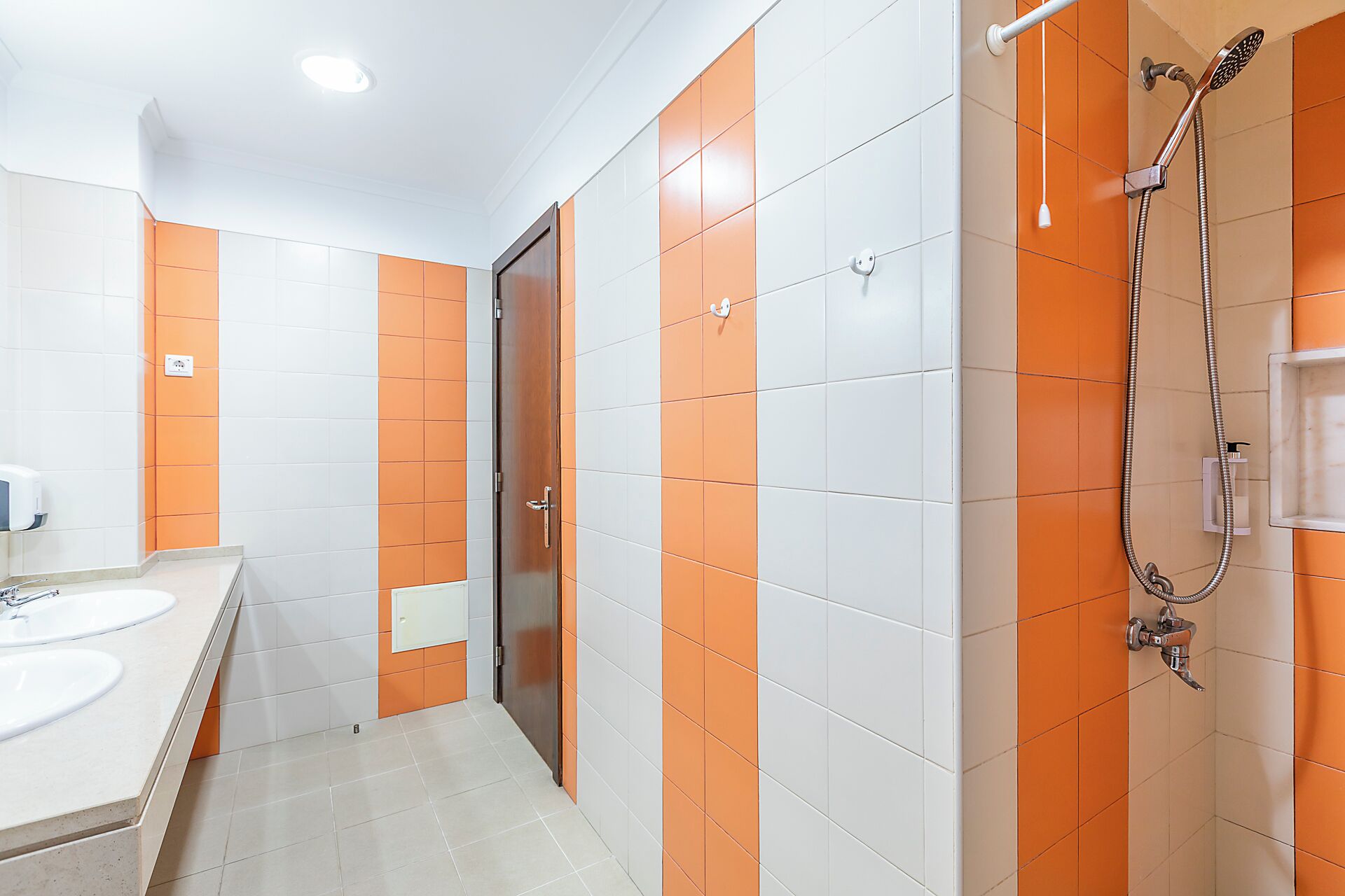Un baño con azulejos blancos y anaranjados, una ducha y un lavamanos con espejo.